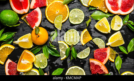 Sliced citrus fruits - grapefruit, orange, tangerine, lemon, lime with leaves . On a black wooden background. Top view Stock Photo