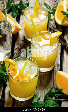 Fresh orange cocktail . Three cocktails from fresh oranges with ice and mint leaves on wooden background Stock Photo
