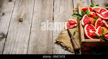 Sliced grapefruit on the Board with a full box and leaves. On wooden background. Free space for text . Stock Photo