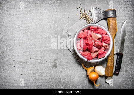 Chopped raw meat with an axe, cutting knife and spices. On the stone table. Free space for text . Top view Stock Photo
