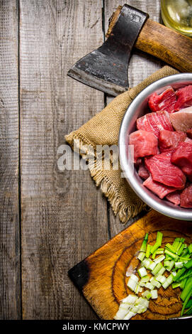 Chopped raw meat with fresh onions and an axe on an old fabric. On a wooden table. Stock Photo