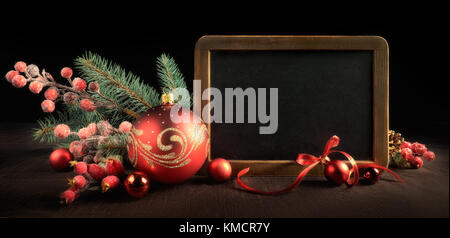 Blackboard with text space surrounded by Christmas decorations on black background. Panoramic framing for banner or web design. Toned image. Top part  Stock Photo