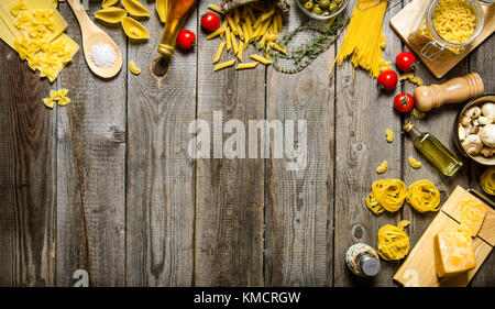 Pasta background. Several types of dry pasta with vegetables, cheese and herbs. On a wooden table.  Free space for text . Top view Stock Photo