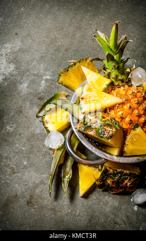 Slices of pineapple from a whole pineapple , leaves and ice in a saucepan. On the stone table. Stock Photo