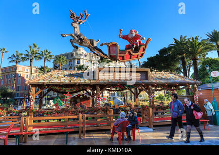 Place Masséna, Nice, France, 5th December 2017. People enjoy a beautifully sunny day with clear blue skies at the Nice Christmas Market. The relaxed atmosphere of the market, with food and gift stalls, children's carousels, colourful lights and a giant ferris wheel beautifully captures the spirit of the Cote d'Azur festive season. Stock Photo