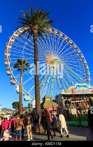 Place Masséna, Nice, France, 5th December 2017. People enjoy a beautifully sunny day with clear blue skies at the Nice Christmas Market. The relaxed atmosphere of the market, with food and gift stalls, children's carousels, colourful lights and a giant ferris wheel beautifully captures the spirit of the Cote d'Azur festive season. Stock Photo