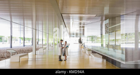 Scientists in lab coats talking in modern office lobby corridor Stock Photo