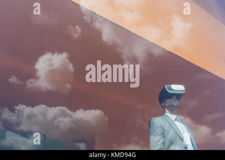 Businessman using virtual reality simulator glasses at window with reflection of clouds Stock Photo