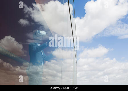 Businessman using virtual reality simulator glasses at window with cloud reflection Stock Photo