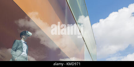 Businessman using virtual reality simulator glasses at modern office window overlooking sunny clouds Stock Photo