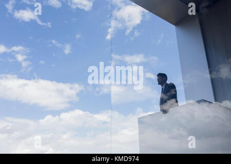 Pensive businessman on modern balcony looking at blue sky and clouds Stock Photo