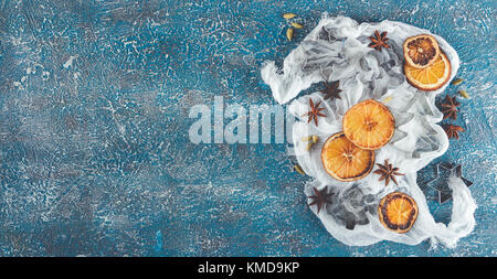 Dried orange slices, cinnamon sticks, anise stars, cardamom seeds in wooden bowls and metal biscuit molds on a blue background Stock Photo