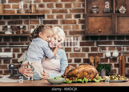 grandmother and granddaughter embracing on kitchen Stock Photo