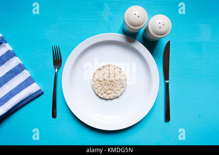 Diet concept. Rice pop cake on a white plate sitting on a blue turquoise wooden table. Table set for light breakfast Stock Photo