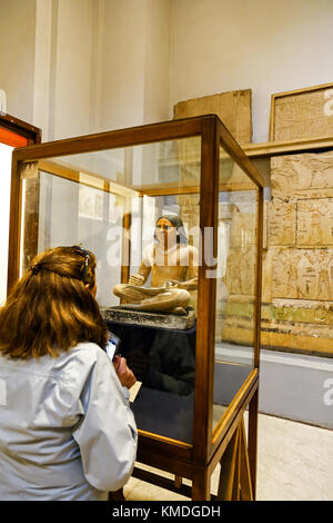 A woman looking at a statue or statuette of a scribe at the Egyptian Museum, Cairo, Egypt, North Africa Stock Photo