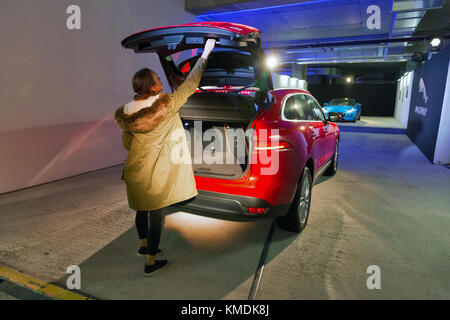 KIEV, UKRAINE - OCTOBER 27, 2017: Young woman with red modern Jaguar F-PACE luxury car with opened empty trunk on the art exhibition Jaguar. The Art o Stock Photo