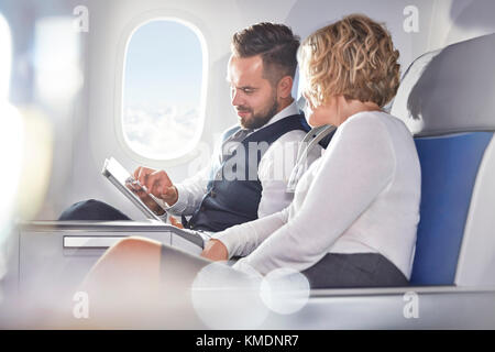 Businessman and businesswoman using digital tablet on airplane Stock Photo