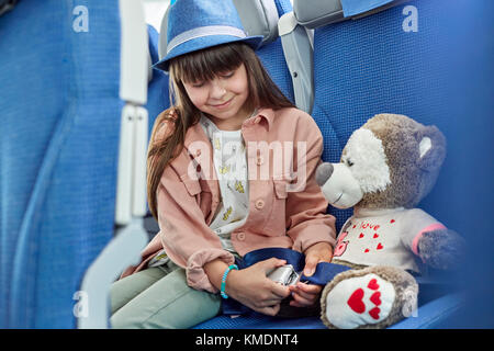 Girl fastening seat belt on stuffed animal on airplane Stock Photo