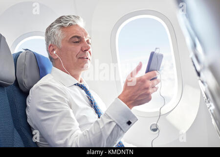 Businessman listening to music with headphones and mp3 player on airplane Stock Photo