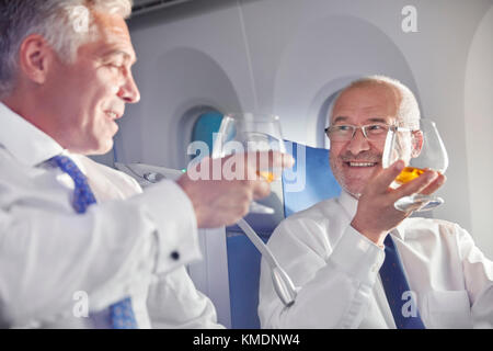 Businessman toasting whiskey glasses in first class on airplane Stock Photo