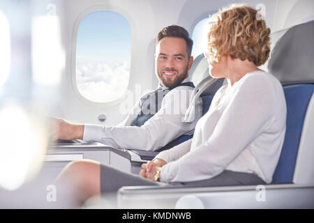 Smiling businessman and businesswoman talking on airplane Stock Photo
