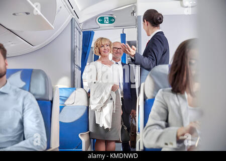 Flight attendant greeting passengers boarding airplane Stock Photo