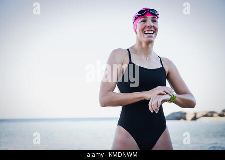 Smiling female open water swimmer adjusting smart watch at ocean Stock Photo