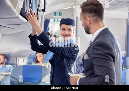 Flight attendant helping businessman with luggage on airplane Stock Photo