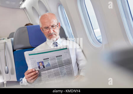 Businessman reading newspaper on airplane Stock Photo