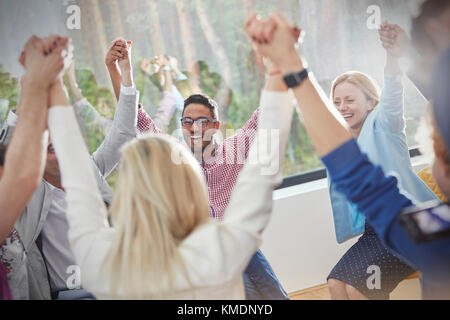 People smiling and holding hands in circle in group therapy session Stock Photo
