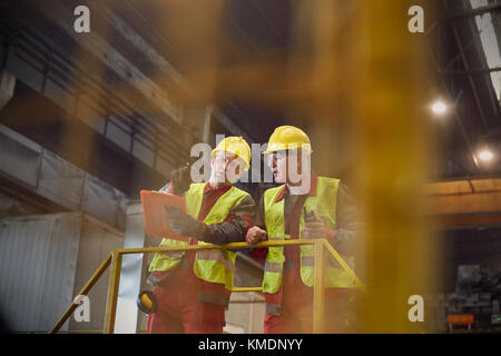 Steelworkers with clipboard talking on platform in steel mill Stock Photo
