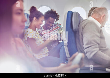 Young couple looking at photos on digital camera on airplane Stock Photo