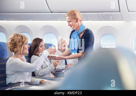 Flight attendant serving drink to woman on airplane Stock Photo