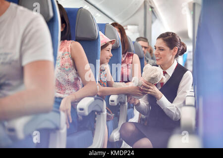 Girl showing teddy bear to female flight attendant on airplane Stock Photo