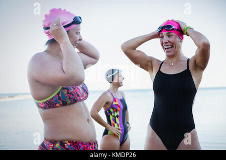 Smiling female open water swimmers adjusting swimming caps at ocean Stock Photo