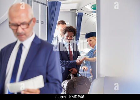 Flight attendant helping businessman with boarding pass on airplane Stock Photo