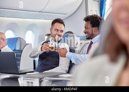 Businessmen toasting whiskey glasses in first class on airplane Stock Photo