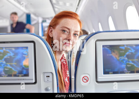 Portrait smiling young woman with red hair and freckles on airplane Stock Photo