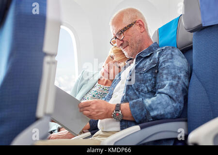 Affectionate mature couple sleeping and reading on airplane Stock Photo