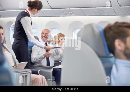 Flight attendant serving whiskey to businessman in first class on airplane Stock Photo