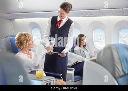 Flight attendant serving champagne to woman in first class on airplane Stock Photo