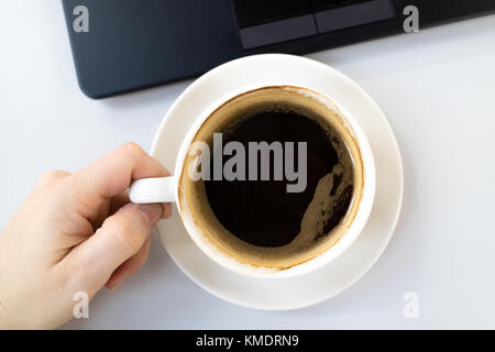 A cup of black coffee in a white mug on a office desk next to a black laptop keyboard Stock Photo