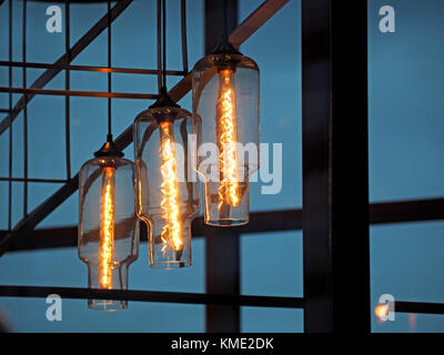 glowing filaments of three decorative incandescent glass lamps in modern setting with black and copper geometric frames in Salford, Manchester,UK Stock Photo