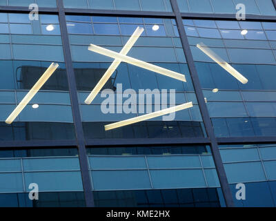 geometric angular pattern of flourescent lights include a cross behind blue glazed facade of modern office building at Salford, Manchester, UK Stock Photo
