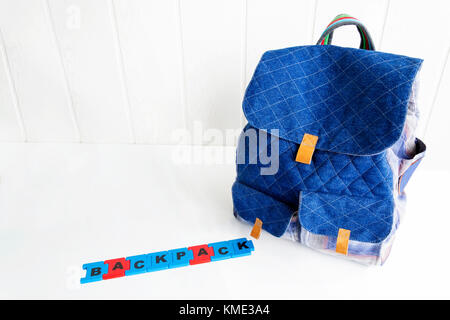 Blue bag with puzzle letters on white table. Hand made backpack for travelers. Stock Photo