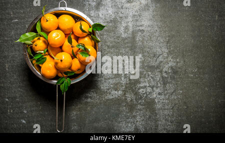 Mandarins with leaves in a saucepan. On a stone background. Free space for text . Top view Stock Photo
