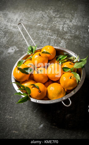 Mandarins with leaves in a saucepan. On a stone background. Stock Photo