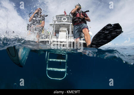 Scuba divers enter water doing giant stride.