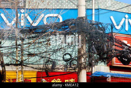 A tangled mess of electric and telephone wires top tall poles through much of central Xian,giving rise to questions re efficient utility administration,distribution,and repair in this part of northeast China.Xi'an,formerly romanized as Sian,and also known as Chang'an before the Ming dynasty,is the capital of Shaanxi Province,People's Republic of China.It is the oldest of the Four Great Ancient Capitals,having held the position under several of the most important dynasties in Chinese history,including Western Zhou,Qin,Western Han,Sui,and Tang. Stock Photo