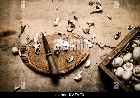 Cutting mushrooms with a knife on an old tree trunk. On wooden background. Stock Photo